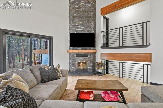 living room featuring light hardwood / wood-style flooring, a high ceiling, beamed ceiling, and a stone fireplace