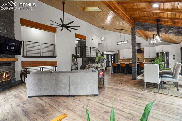 living room featuring light wood-type flooring, ceiling fan with notable chandelier, high vaulted ceiling, and a fireplace