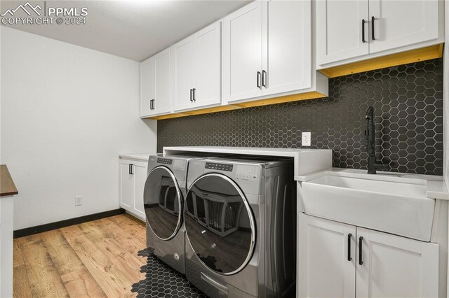 clothes washing area featuring light wood-type flooring, washing machine and clothes dryer, cabinets, and sink