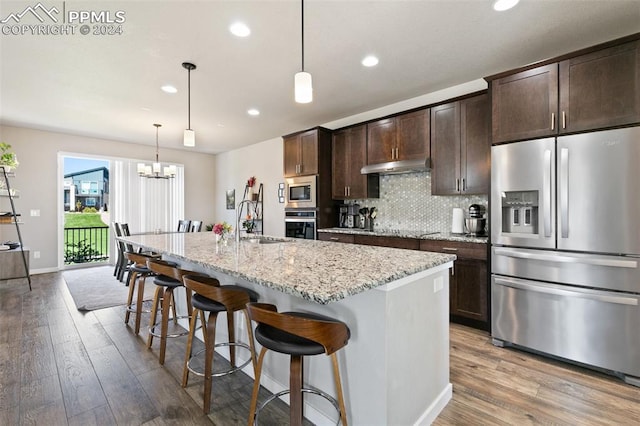 kitchen featuring light hardwood / wood-style flooring, appliances with stainless steel finishes, light stone countertops, a kitchen bar, and a kitchen island with sink