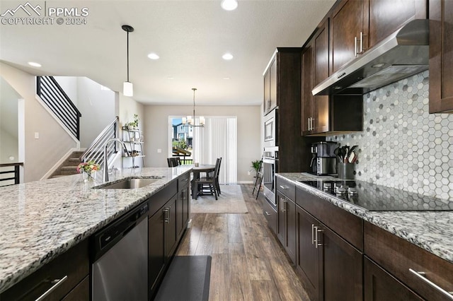 kitchen with an inviting chandelier, stainless steel appliances, sink, hardwood / wood-style flooring, and light stone counters