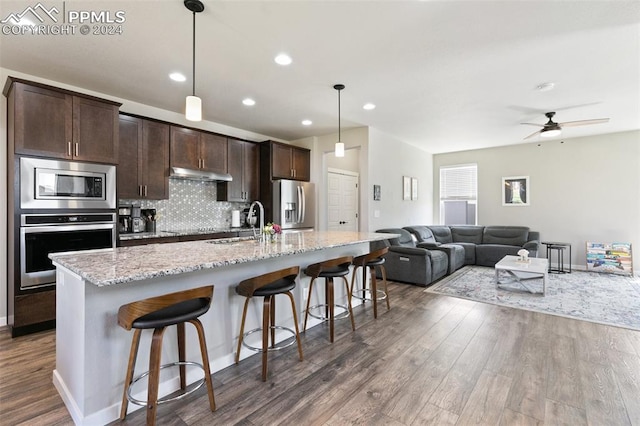 kitchen featuring a kitchen bar, dark wood-type flooring, stainless steel appliances, an island with sink, and ceiling fan