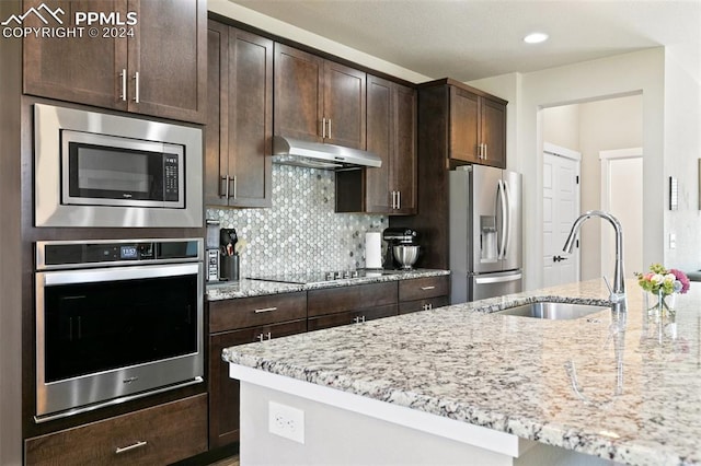 kitchen featuring dark brown cabinets, backsplash, stainless steel appliances, light stone counters, and sink