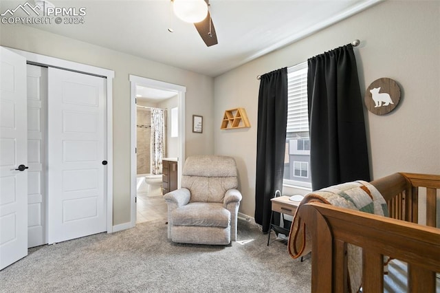 bedroom featuring connected bathroom, light carpet, ceiling fan, and a crib