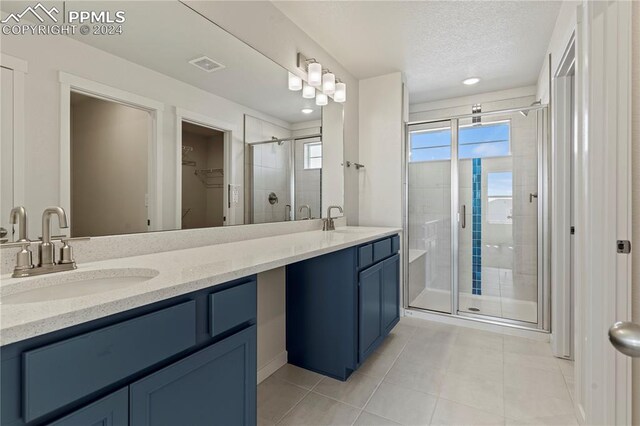 bathroom featuring a shower with door, vanity, tile patterned floors, and a textured ceiling