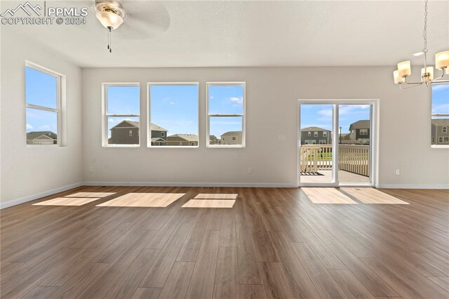 unfurnished living room featuring a wealth of natural light, dark hardwood / wood-style floors, and ceiling fan with notable chandelier