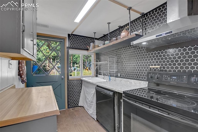 kitchen with butcher block countertops, wall chimney exhaust hood, black appliances, gray cabinets, and light wood-type flooring