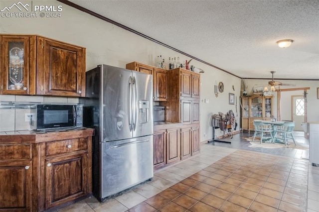 kitchen with ceiling fan, lofted ceiling, light tile patterned floors, a textured ceiling, and stainless steel refrigerator with ice dispenser