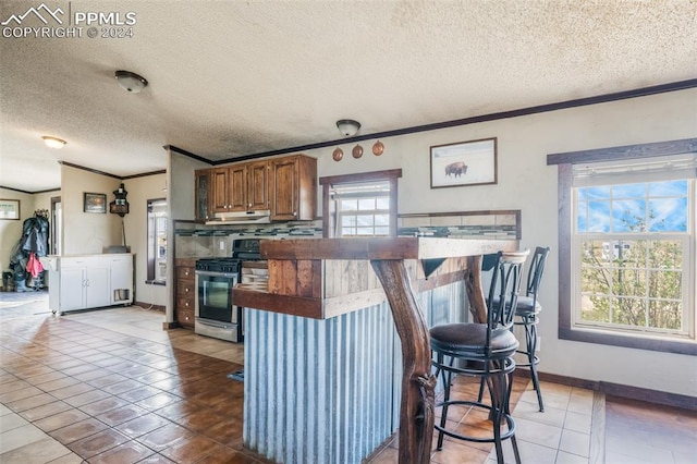 kitchen featuring light tile patterned floors, a textured ceiling, stainless steel range oven, crown molding, and decorative backsplash