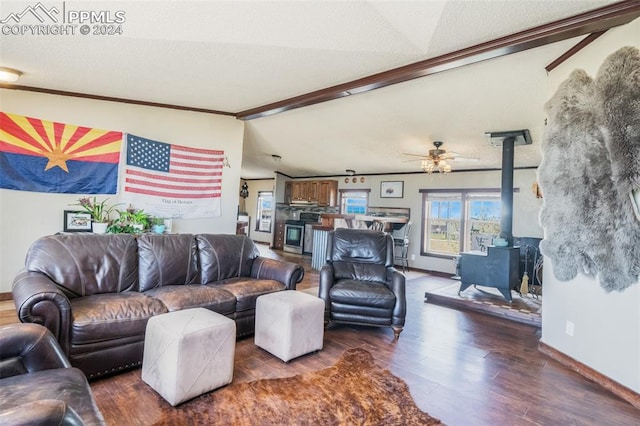 living room featuring ceiling fan, vaulted ceiling with beams, ornamental molding, a wood stove, and dark wood-type flooring