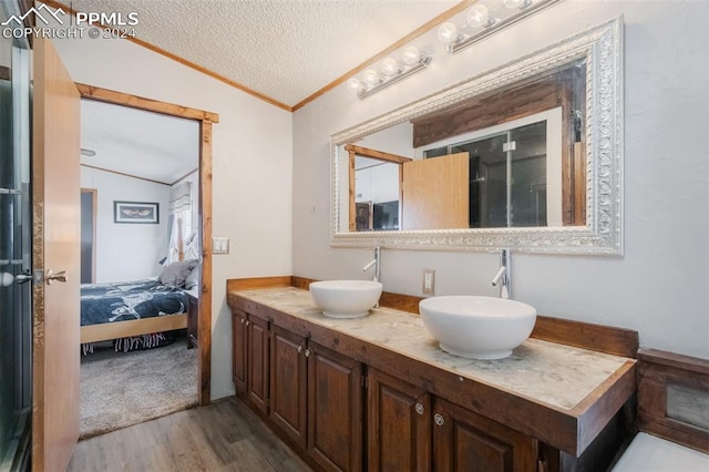 bathroom with vaulted ceiling, vanity, a textured ceiling, crown molding, and hardwood / wood-style flooring