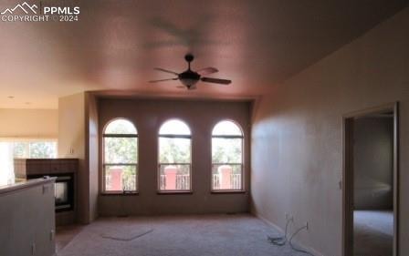 unfurnished living room featuring light colored carpet, ceiling fan, and a fireplace