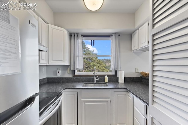 kitchen featuring stainless steel range, refrigerator, sink, and white cabinets