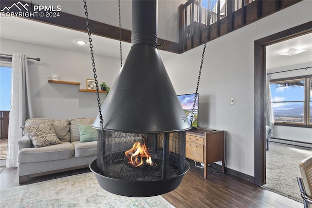 living room featuring a multi sided fireplace, dark hardwood / wood-style flooring, a wood stove, beam ceiling, and a baseboard heating unit