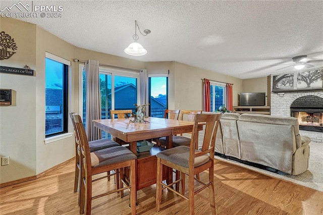 dining room with ceiling fan, a textured ceiling, light hardwood / wood-style flooring, and a fireplace