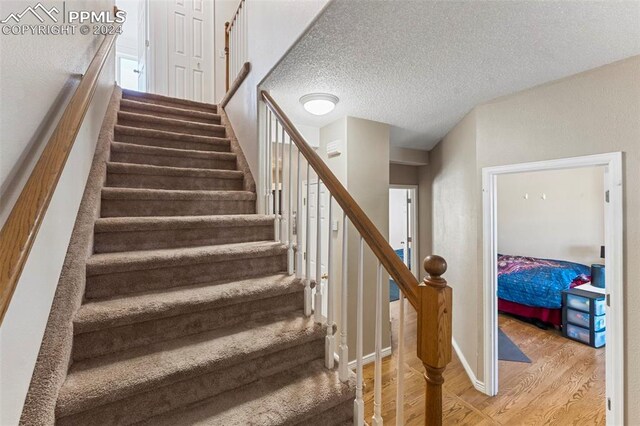 stairway with a textured ceiling and wood-type flooring