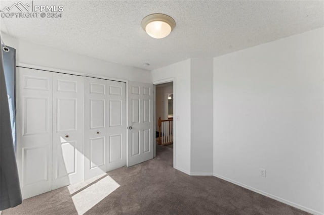 unfurnished bedroom with dark colored carpet, a closet, and a textured ceiling