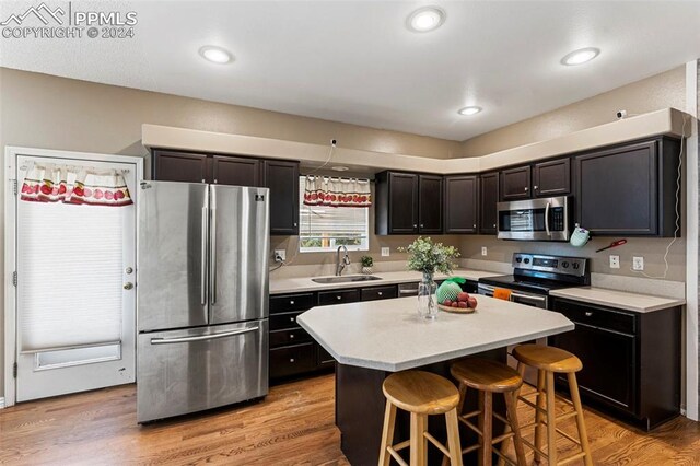 kitchen with a kitchen breakfast bar, stainless steel appliances, a center island, light hardwood / wood-style flooring, and sink