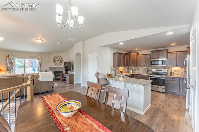 kitchen with light stone countertops, backsplash, stainless steel appliances, kitchen peninsula, and light wood-type flooring