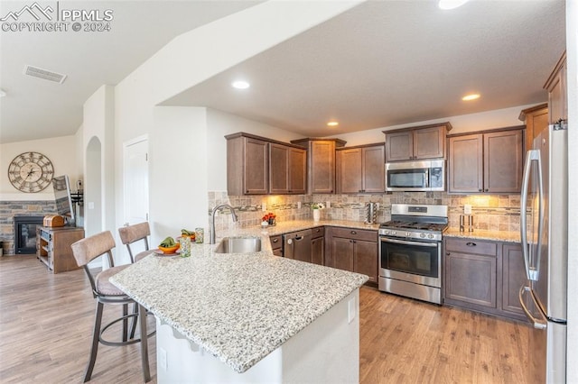 kitchen with a kitchen bar, kitchen peninsula, sink, a stone fireplace, and appliances with stainless steel finishes