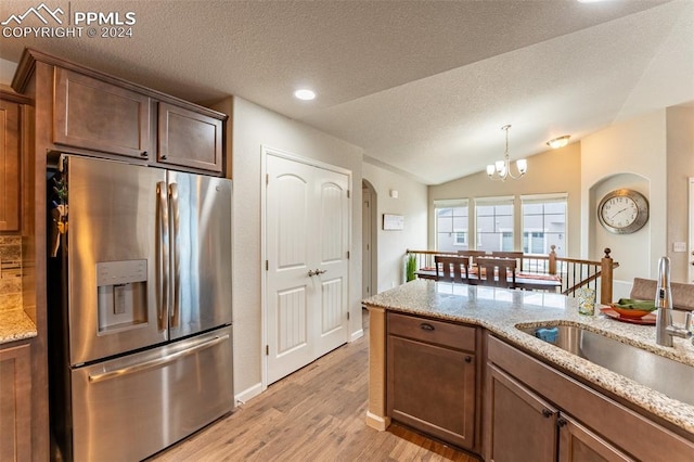 kitchen with light wood-type flooring, light stone counters, sink, stainless steel fridge, and a textured ceiling