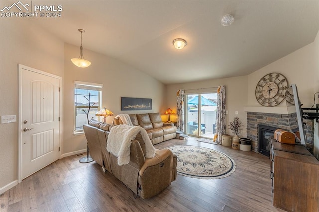 living room with lofted ceiling, a wealth of natural light, wood-type flooring, and a stone fireplace