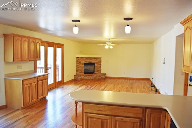 kitchen with decorative light fixtures, ceiling fan, a fireplace, and light hardwood / wood-style flooring