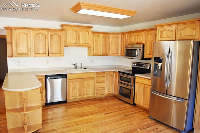 kitchen with appliances with stainless steel finishes, sink, light brown cabinets, and light hardwood / wood-style floors