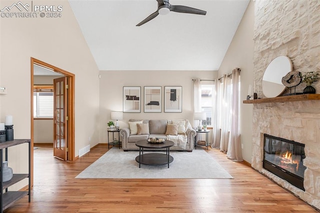 living room featuring light hardwood / wood-style flooring, ceiling fan, high vaulted ceiling, and a stone fireplace