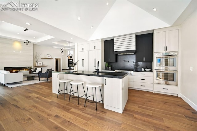 kitchen featuring a large island with sink, a large fireplace, light hardwood / wood-style floors, and white cabinetry