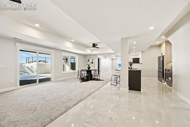 interior space with ceiling fan, stainless steel appliances, a breakfast bar area, light carpet, and white cabinets