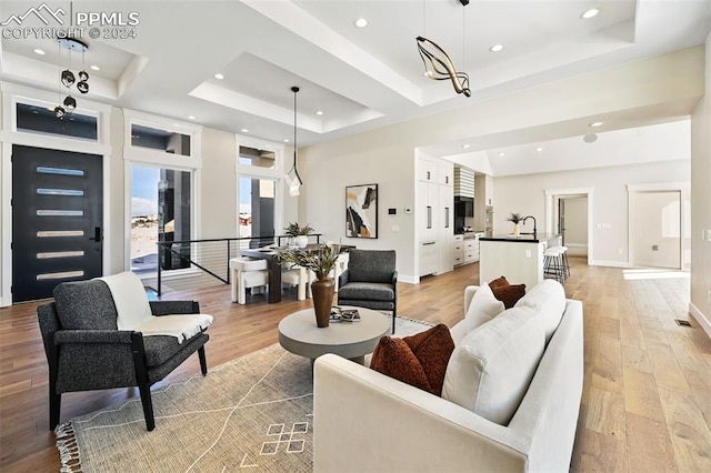 living room featuring a chandelier, light hardwood / wood-style floors, a raised ceiling, and sink