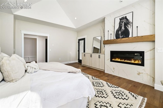 bedroom featuring a large fireplace, dark wood-type flooring, and vaulted ceiling