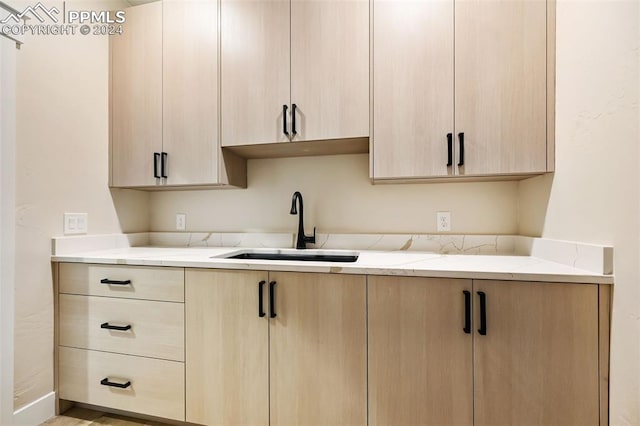 kitchen with light brown cabinetry, light stone counters, and sink