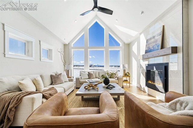 living room with a tile fireplace, light wood-type flooring, high vaulted ceiling, and ceiling fan