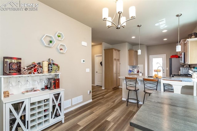 kitchen featuring pendant lighting, a notable chandelier, wood-type flooring, kitchen peninsula, and light brown cabinets