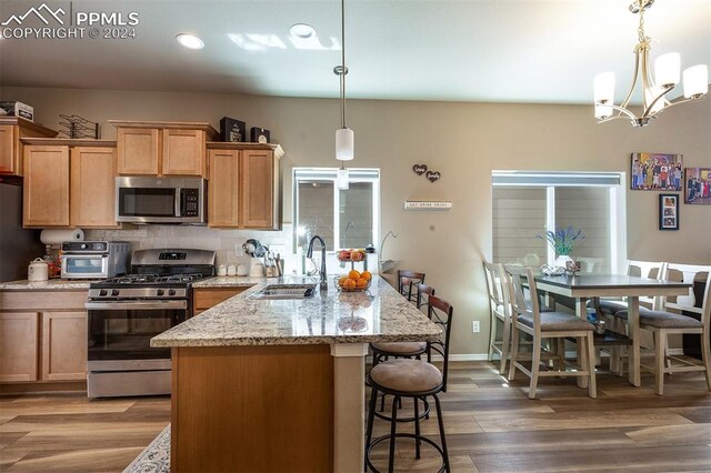 kitchen featuring an inviting chandelier, wood-type flooring, appliances with stainless steel finishes, sink, and light stone counters