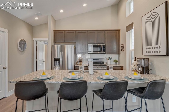 kitchen featuring a kitchen breakfast bar, stainless steel appliances, light hardwood / wood-style floors, and vaulted ceiling