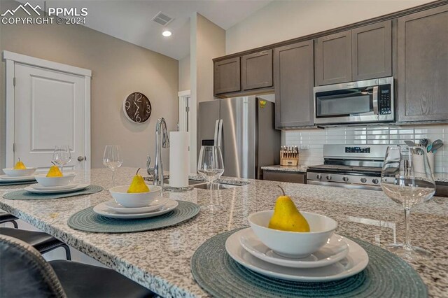 kitchen featuring appliances with stainless steel finishes, light stone countertops, decorative backsplash, and dark brown cabinetry