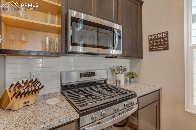 kitchen with light stone countertops, appliances with stainless steel finishes, dark brown cabinets, and tasteful backsplash