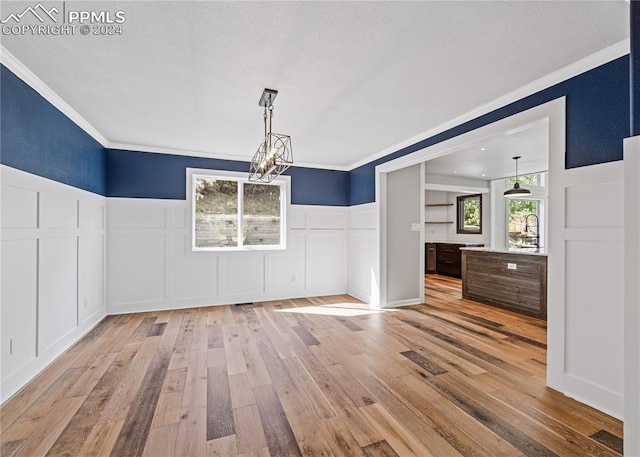 unfurnished dining area featuring a notable chandelier, light wood-type flooring, and crown molding