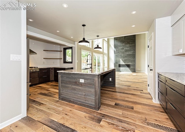 kitchen with pendant lighting, an island with sink, dark brown cabinets, light hardwood / wood-style flooring, and a breakfast bar