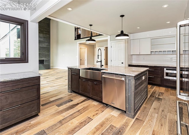 kitchen with an island with sink, light wood-type flooring, sink, hanging light fixtures, and appliances with stainless steel finishes