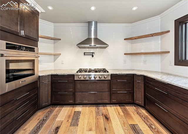 kitchen with light stone counters, tasteful backsplash, wall chimney exhaust hood, appliances with stainless steel finishes, and light wood-type flooring