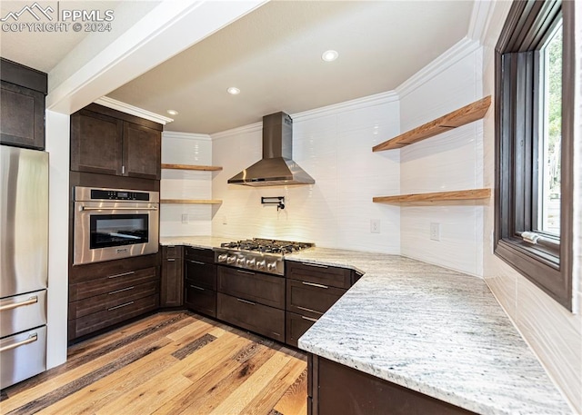 kitchen featuring wall chimney range hood, light wood-type flooring, stainless steel appliances, light stone countertops, and ornamental molding