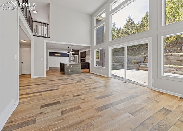 unfurnished living room featuring a towering ceiling and light hardwood / wood-style flooring