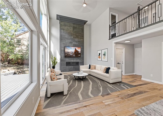 living room featuring a towering ceiling, ceiling fan, light wood-type flooring, and a tiled fireplace