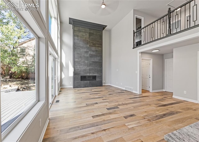 living room with ceiling fan, a fireplace, light hardwood / wood-style floors, and a high ceiling