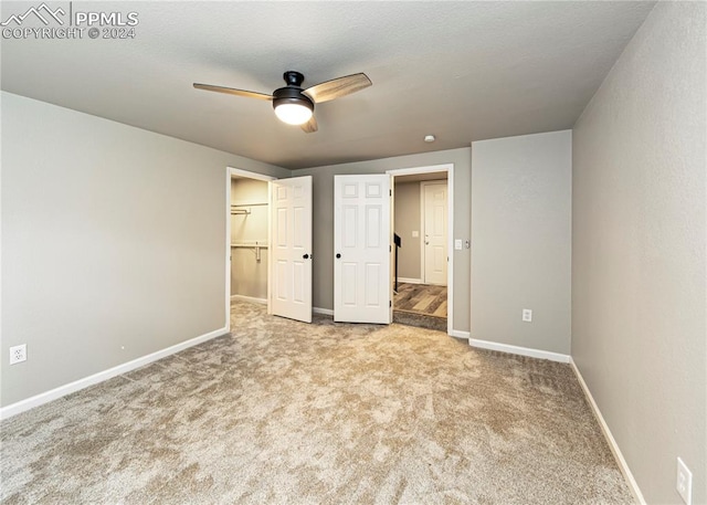 unfurnished bedroom with a closet, light colored carpet, a walk in closet, and ceiling fan