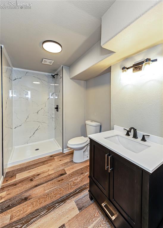 bathroom with hardwood / wood-style floors, toilet, tiled shower, and vanity